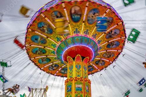 Um brinquedo grande e colorido no parque de diversões com poucas pessoas, em um dia nublado. Foto feita de baixo para cima.