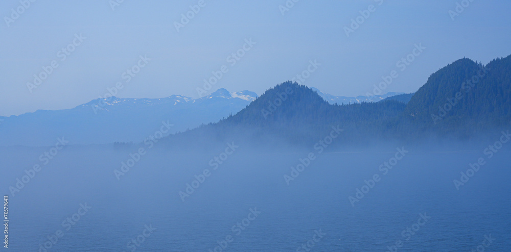 View of snow capped mountains appearing above a sea of clouds in the Inside Passage of Southeastern Alaska in the Pacific Ocean, USA