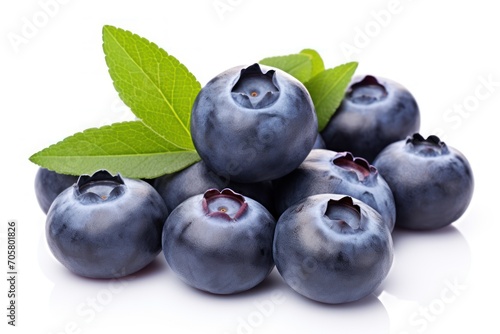  a pile of blueberries with a green leaf on top of one of the blueberries is on a white surface with a reflection on the bottom of the image.