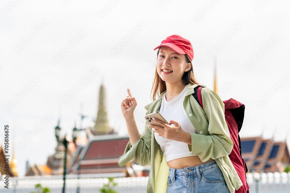 Young asian woman traveler with phone capturing moments and exploring Wat Phra Kaew and The Grand Palace in a happy and casual style during a sunny day