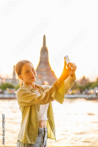 Young Asian Woman Traveler Taking a Selfie While Enjoying The Sunset Moments of Wat Arun by the Chao Phraya Riverbank in Bangkok, Thailand © asean studio