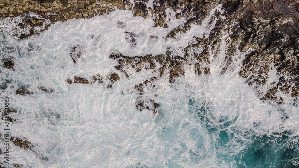 Drone view of Atlantic ocean waves meet with underwater pointed rocky. Blue rough sea with big waves with foam crashing against the rocks, south of Tenerife, Canary island