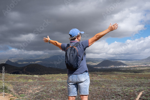 Back view of senior woman walking on hiking day on outdoor trail on countryside excursion. Caucasian woman with outstretched arms enjoying adventure or retirement leading healthy lifestyle.