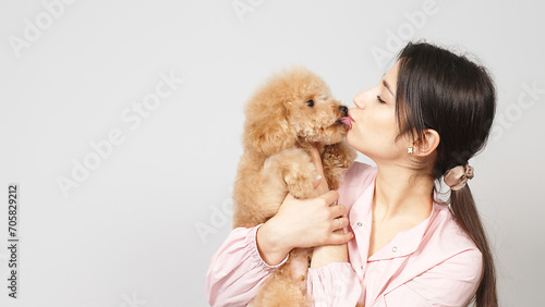 A cute and caring groomer or veterinarian hugs a little poodle puppy. Concept of caring for pets and treating them well. Place for text.