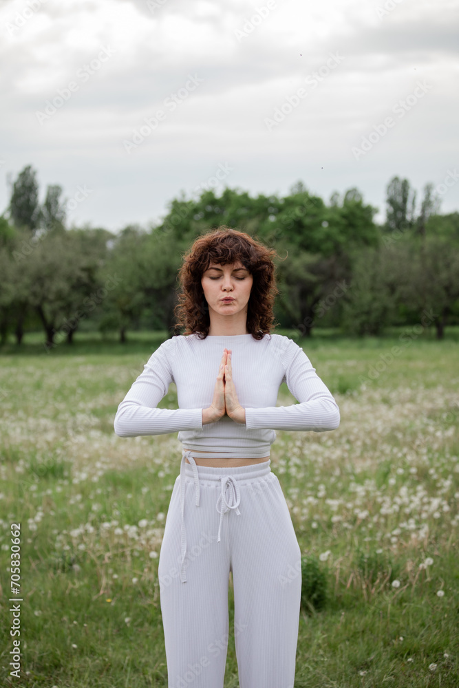 Concept of meditation on fresh air. Young lady practicing namaste gesture greetings outdoors. Female in white clothes warm up before breath aerobics training. Sports woman folded palms together Concept of meditation on fresh air. Young lady practicing namaste gesture greetings outdoors. Female in white clothes warm up before breath aerobics training. Sports woman folded palms together