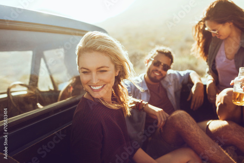 Group of friends laughing and drinking beer at the back of a car on a road trip photo