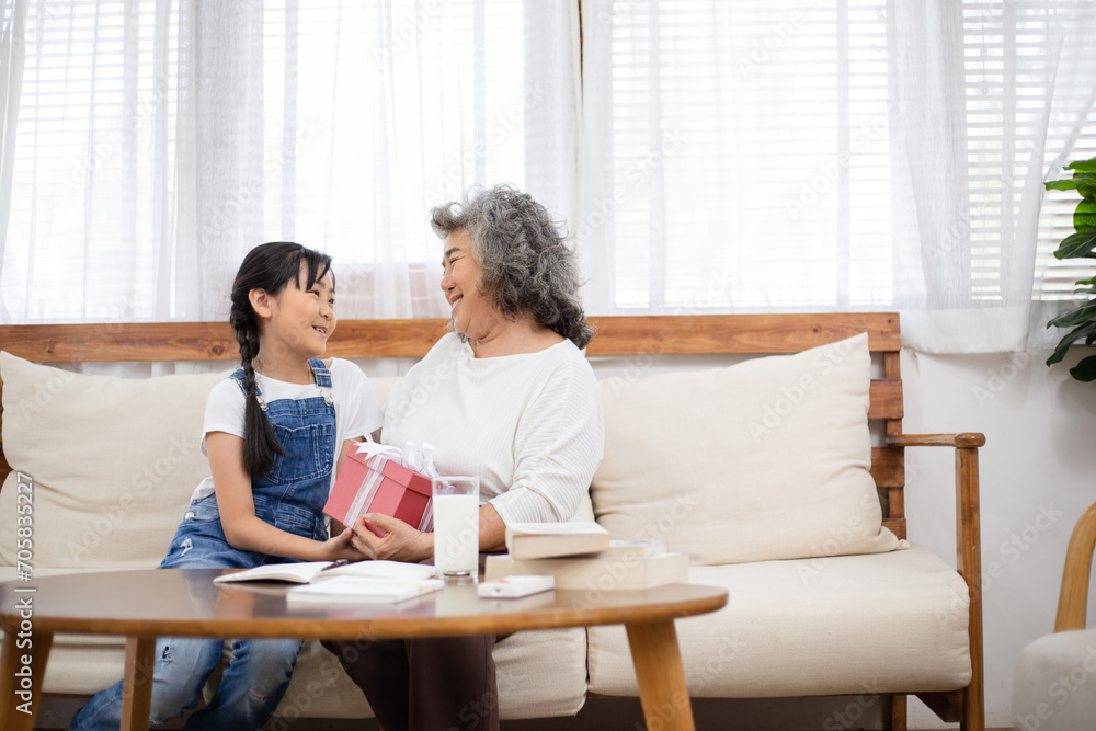 Asian girl surprise and giving her grandmother a present box. Granddaughter visit senior woman on holidays weekend. Family meeting, bonding relationship. Healthy living insurance after retired Asian girl surprise and giving her grandmother a present box. Granddaughter visit senior woman on holidays weekend. Family meeting, bonding relationship. Healthy living insurance after retired