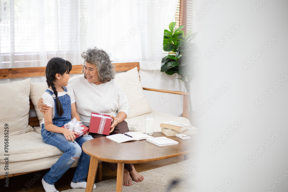 Asian girl surprise and giving her grandmother a present box. Granddaughter visit senior woman on holidays weekend. Family meeting, bonding relationship. Healthy living insurance after retired Asian girl surprise and giving her grandmother a present box. Granddaughter visit senior woman on holidays weekend. Family meeting, bonding relationship. Healthy living insurance after retired