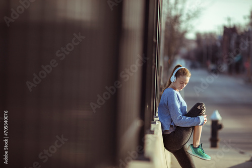Young female athlete with headphones stretching in city street