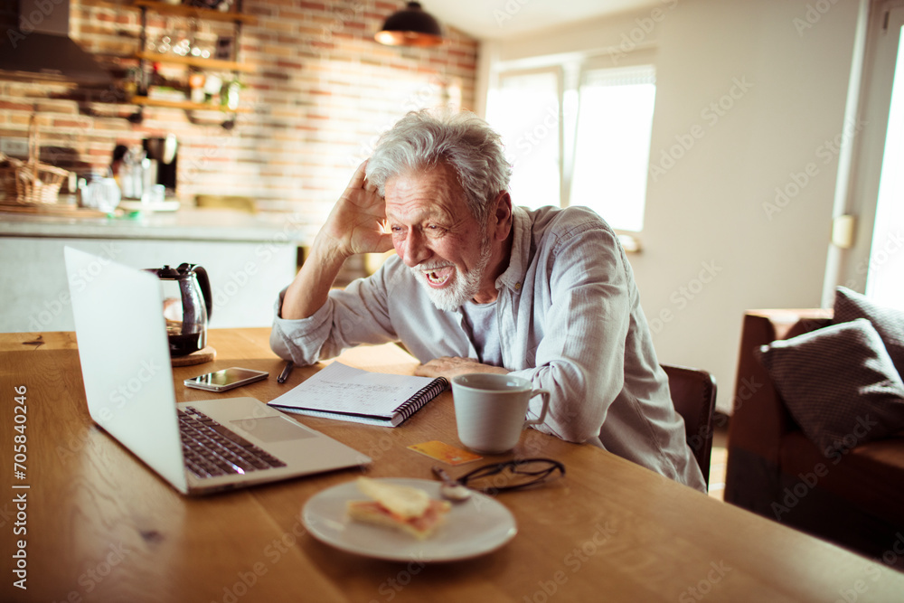 Senior man working at home with laptop and papers on desk Senior man working at home with laptop and papers on desk