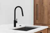 A kitchen sink detail with a black faucet, white marble countertop, and wood cabinets with black hardware.