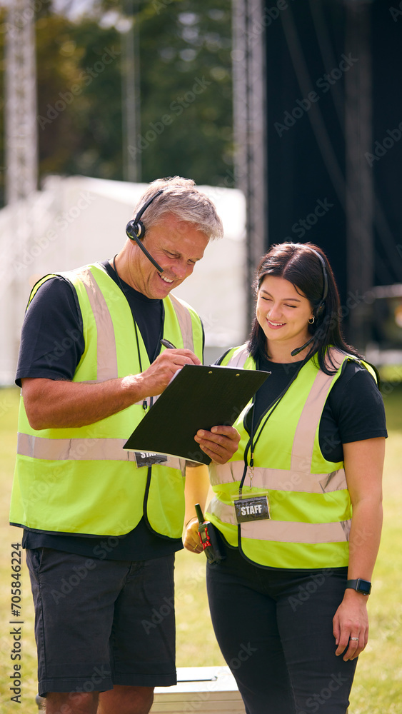 Male And Female Production Team With Headsets Setting Up Outdoor Stage For Music Festival Or Concert Male And Female Production Team With Headsets Setting Up Outdoor Stage For Music Festival Or Concert