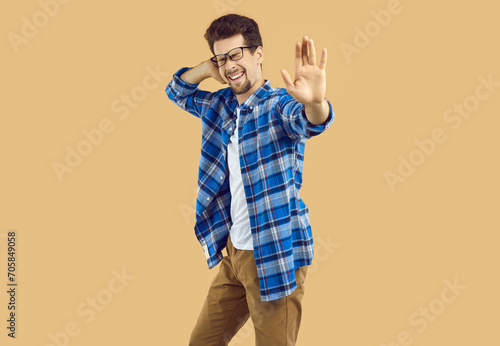 Cheerful cool excited funny young man happily dancing. Happy handsome bearded man wearing eyeglasses and casual clothes having fun over isolated beige studio background