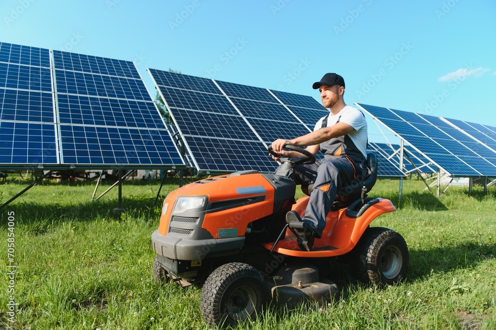 Fototapeta premium A man mows the grass near the solar panels. Green energy