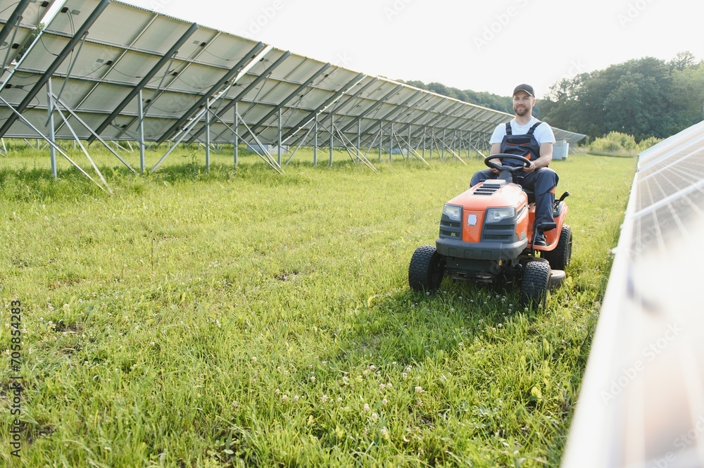 A man working at solar power station. A worker on a garden tractor mows grass on a solar panel farm. A man working at solar power station. A worker on a garden tractor mows grass on a solar panel farm.