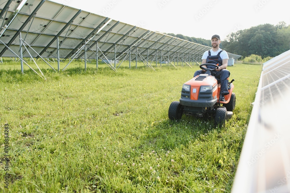 A man working at solar power station. A worker on a garden tractor mows grass on a solar panel farm.