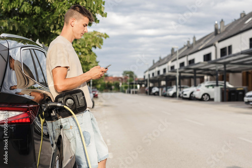 Man in a casual summer outfit, charging electric car parked on the street. Green and sustainable energy. © 24K-Production