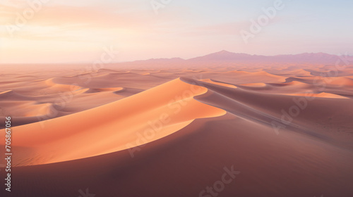 Drone photograph of a vast desert landscape with rolling sand dunes at sunrise.