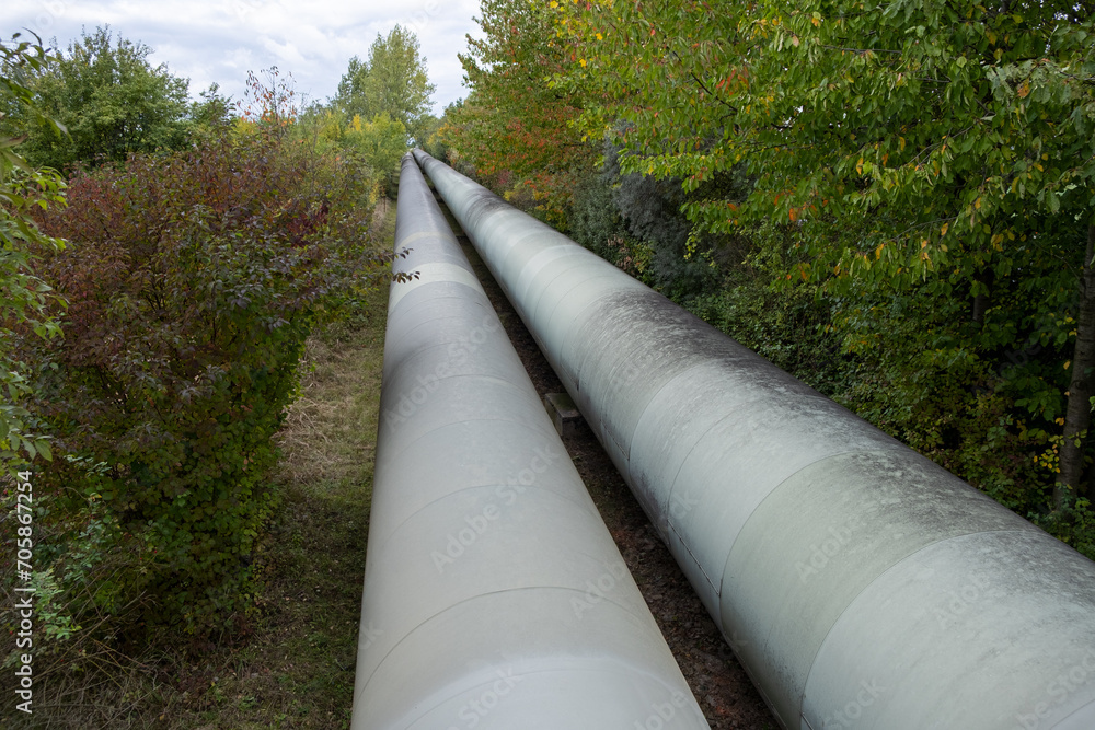 A colossal tube represents a thermal energy transfer infrastructure, central heating pipes enveloped in a robust metal thermal insulation jacket. Above-ground in European regions distribution energy A colossal tube represents a thermal energy transfer infrastructure, central heating pipes enveloped in a robust metal thermal insulation jacket. Above-ground in European regions distribution energy