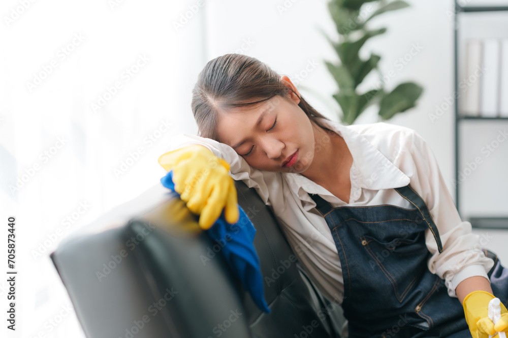 Young Asian woman tired from doing housework. Asian female housewife who is tired from cleaning the house sits with her back the sofa. Young Asian woman tired from doing housework. Asian female housewife who is tired from cleaning the house sits with her back the sofa.