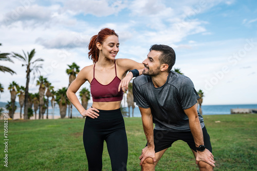 Relaxed young adult couple looking each other after running together in the park. Affectionate satisfied athletic male and female in sportswear training workout outside.