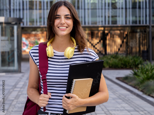 Portrait of a smiling Caucasian teenage student girl with a backpack and folder looking at camera.