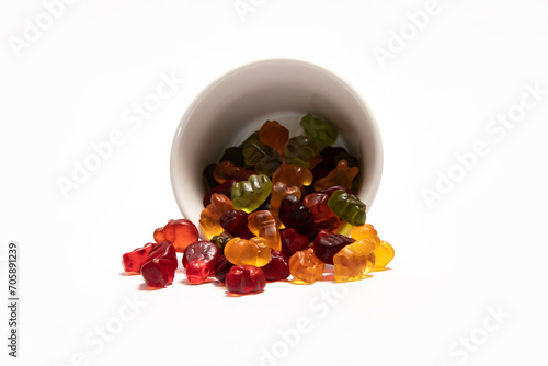 Colorful gummy candies spiled from the white cup on white background photo