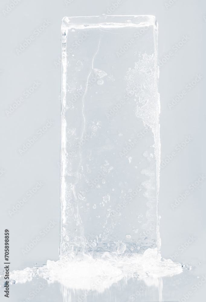 Crystal clear natural ice block in light blue tones on a white reflective surface. Crystal clear natural ice block in light blue tones on a white reflective surface.