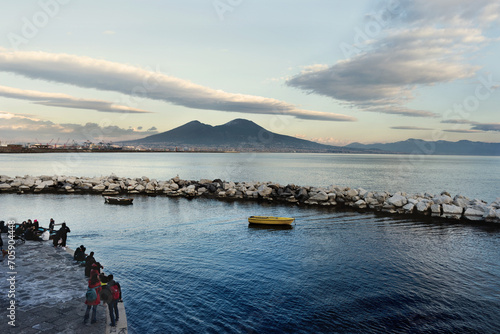 il Vesuvio visto dal lungomare di Mergellina, prospettiva con persone, barche e scogliera sullo sfondo, mare blu, e nuvole in movimento, vulcano dei campi flegrei, bellezza della natura, Napoli   photo