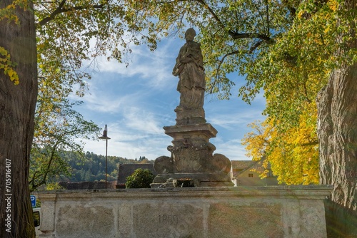 Svojsin  Czech Republic - October 13 2023  View of the stone water fountain with Johannes Nepomuk statue surrounded by yellow and green leaves. Sunny autumn day with blue sky.