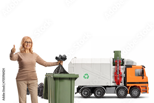 Woman in front of a garabe truck throwing a waste bag in a bin and gesturing thumbs up photo