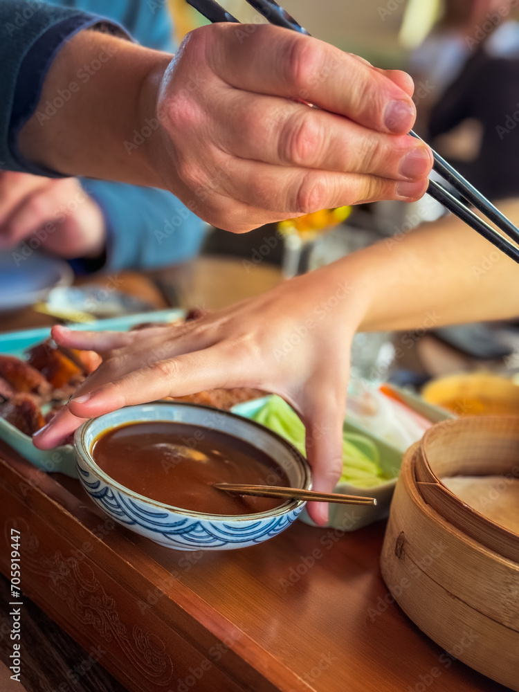 Obraz premium woman's hand and man's hand with chopsticks preparing a duck roll served Asian-style with vegetables and sauce