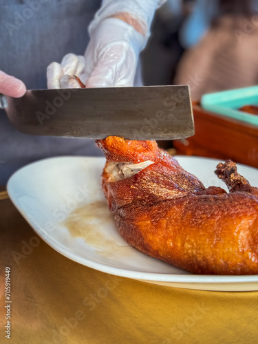 preparation of the lacquered duck by the cook for serving at the table, with a large knife and gloves, Asian style