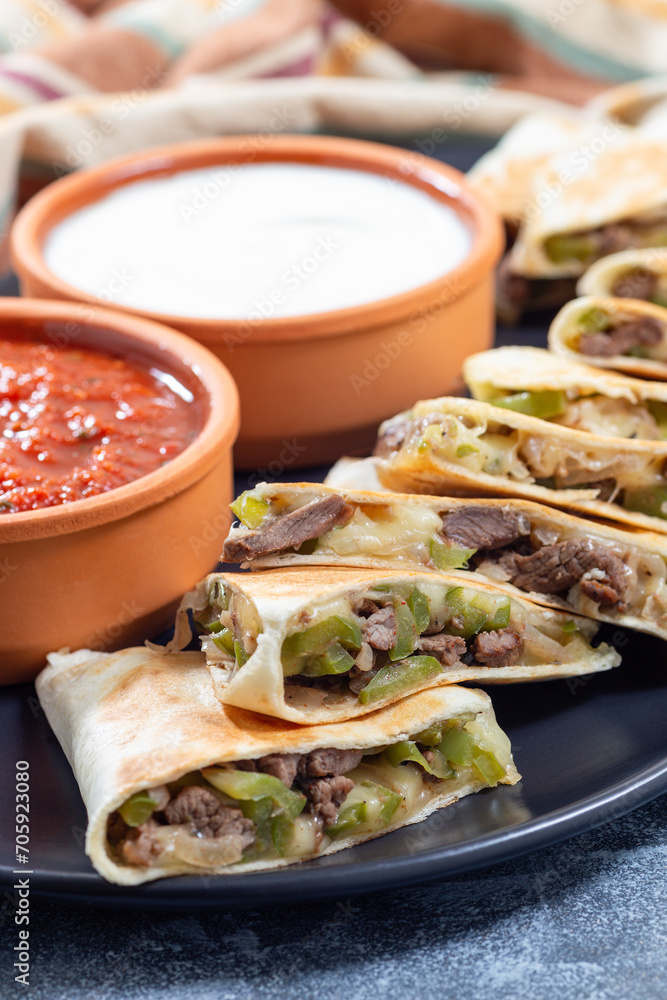 Fajita quesadilla with pieces of beef steak, green bell pepper, onion and cheese, on plate, closeup