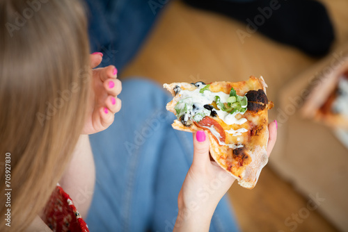 The girl holds an over-eaten piece of salami pizza in her hand.