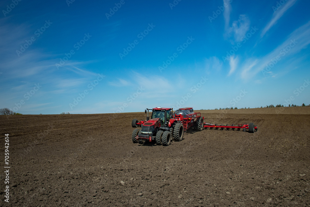 Naklejka premium Red tractor with a planter sowing corn in the field