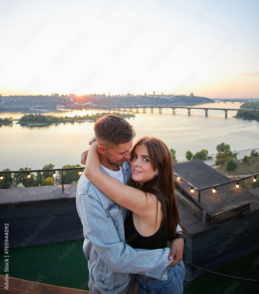 A young couple enjoys a serene evening on a rooftop, surrounded by the warm hues of a setting sun.
