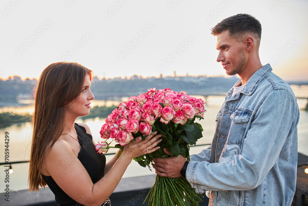 A young man presents a massive bouquet of roses to his beloved