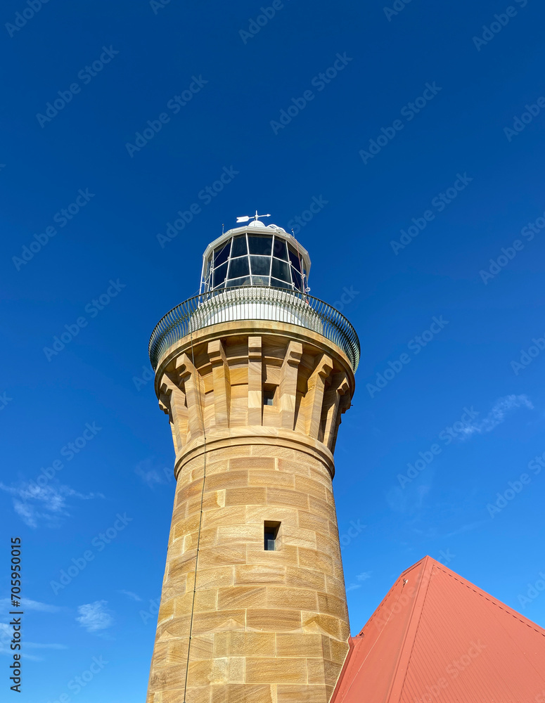 Lighthouse on the island at daytime. Sandstone lighthouse at the top of a hill. Coast lighthouse against a blue sky in the harbor. Lighthouse on the coast of the region sea.