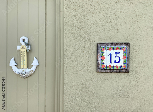 Fifteen. Number fifteen on a wall and an anchor-shaped external thermometer. Address made with ceramic tiles with red rose pattern on a house wall. Concept of the number 15. Sign and symbol, font.