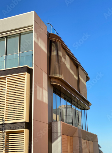 Modern building facade with balconies and windows against blue sky. Close-up of architectural structural details. Facade with wooden panels for shade.