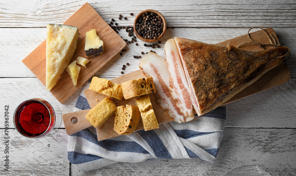 Savory biscuit with pecorino, guanciale and pepper. Cutting board with Italian rustic snack and red wine glass on white wooden background. close-up.