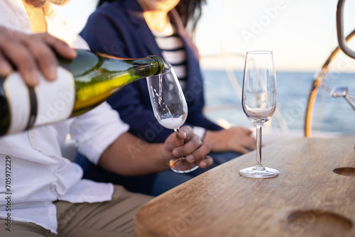 Crop couple pouring champagne into wineglasses on yacht photo