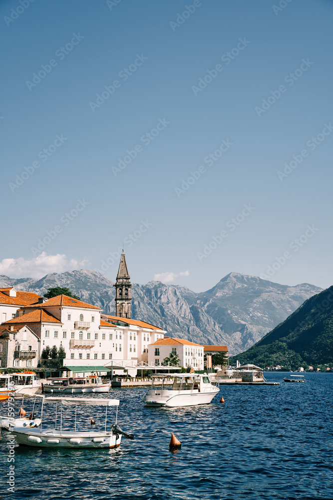 Excursion boats are moored off the coast of Perast with ancient houses and a church bell tower. Montenegro