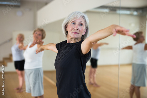 Portrait of athletic european aged woman doing stretching warm-up during group workout at gym .