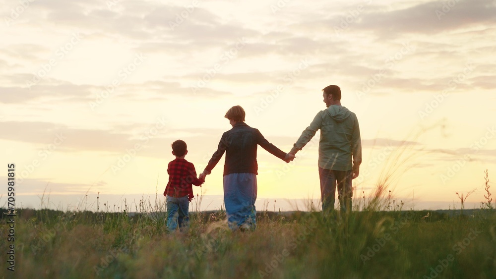 Family silhouettes joining hands with love walk along grassy valley basking in serenity of landscape. Family lovely walks in grassy valley. Family creating heartwarming family moment walking on field