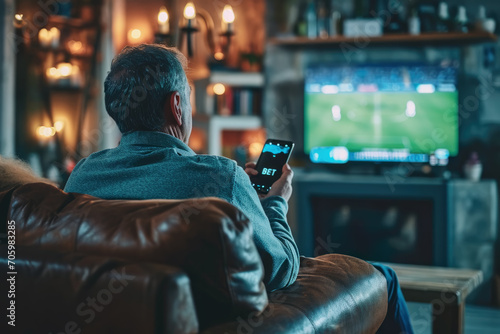 Senior Male Looking at Smartphone in Living Room and Making Sport Bet.