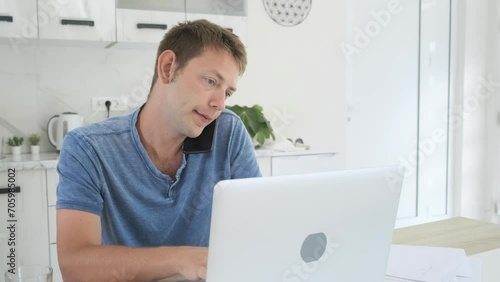 Serious businessman trader talking on phone call while work on laptop at home. Male professional broker investor working online on stock market and crypto currency with smartphone and computer photo