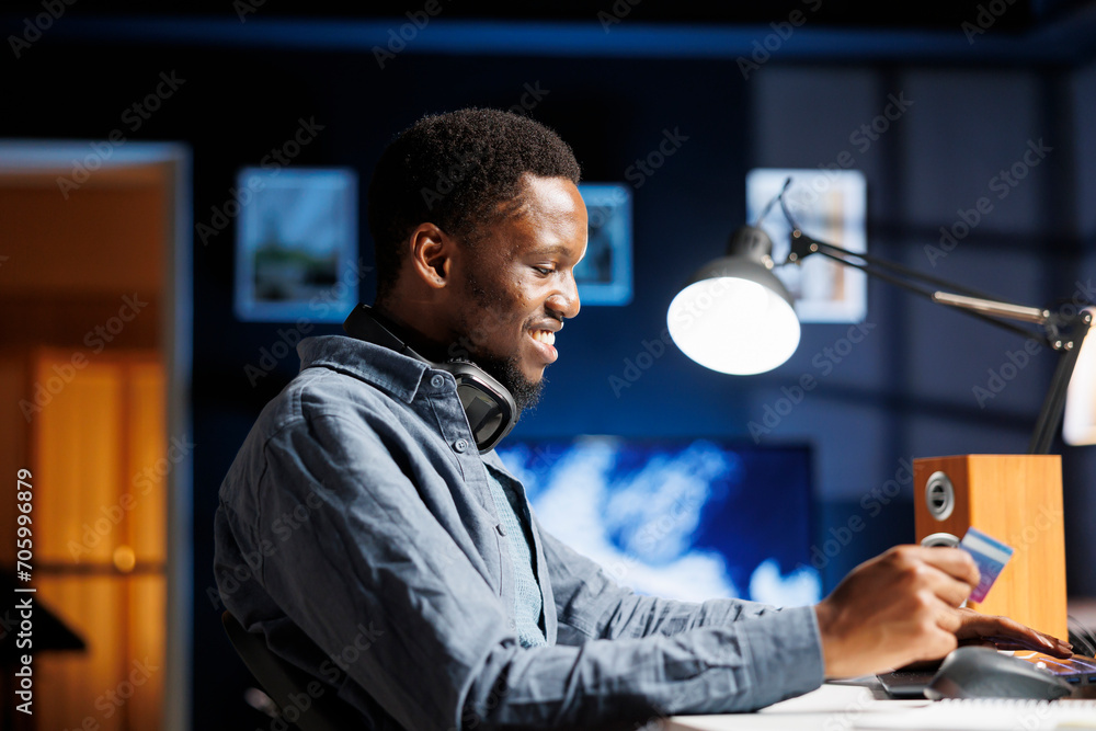 Optimist purchasing clothes on an online store and entering credit card information to complete digital payment. African american person shopping on discount, paying with financial services data. Optimist purchasing clothes on an online store and entering credit card information to complete digital payment. African american person shopping on discount, paying with financial services data.