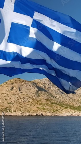 Greek flag waving against an island and a passing sailing boat - symbols of Greece